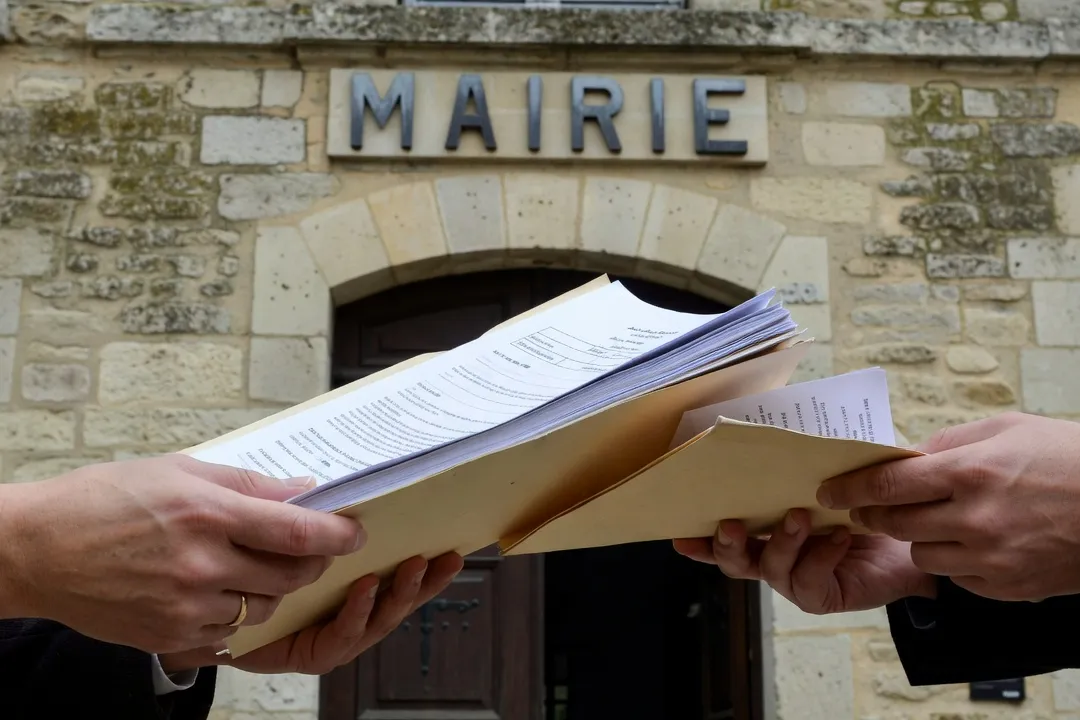 Couple's hands holding a folder of legal documents near a French mairie building
